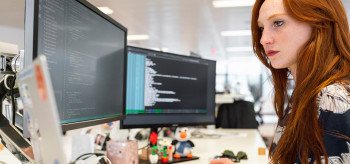 A lady programmer is doing coding for software development with three monitors on her desk, A beautiful programmer using three monitors for coding software,