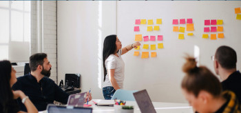 A Group of people is discussing and one of them is providing guidelines on several IT-related colorful notes from the whiteboard, Team members are discussing consultancy service,