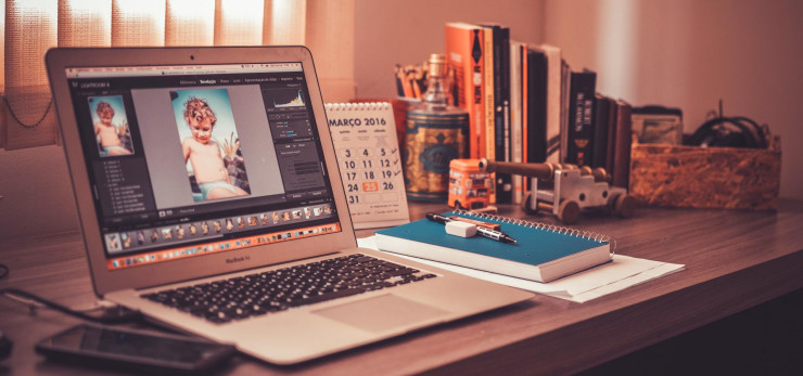 A laptop featuring graphical and photoshop design on a table with several books and tools, A laptop computer with several books and accessories,