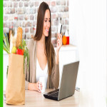 A beautiful lady is sitting with a laptop holding a pen in her left hand and a coffee mug in her right hand, A lovely lady sitting with a laptop and a shopping bag in her right,